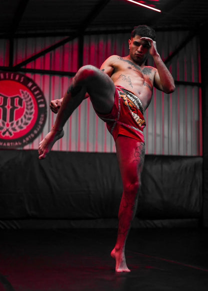 Professional Muay Thai fighter kicking in red and green MMA shorts