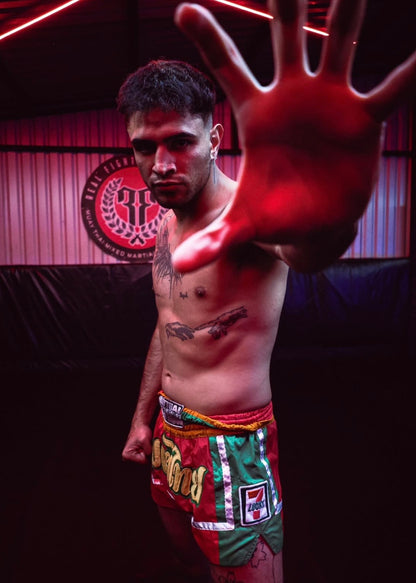 Aldo “Hit-Boy” Cruz modelling red, orange, and green Muay Thai shorts