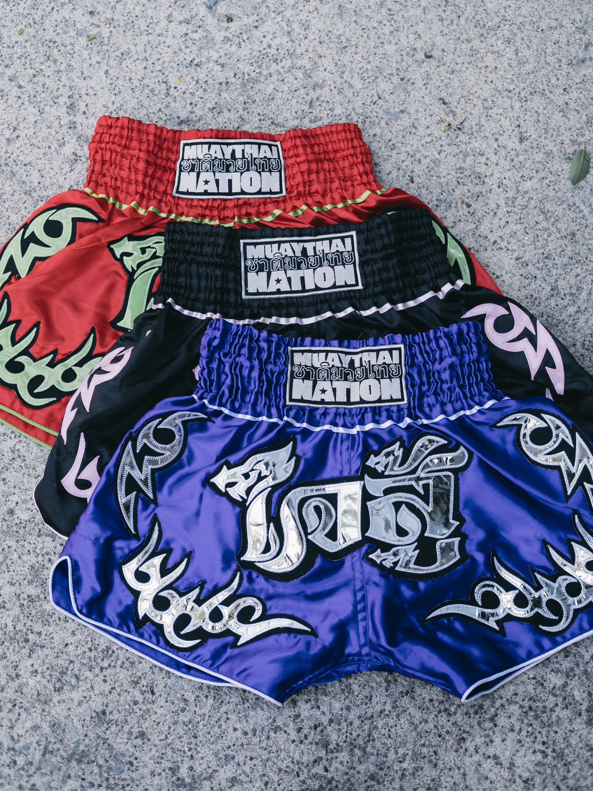 Collection of blue, red, black Muay Thai shorts with muay thai nation logo. 