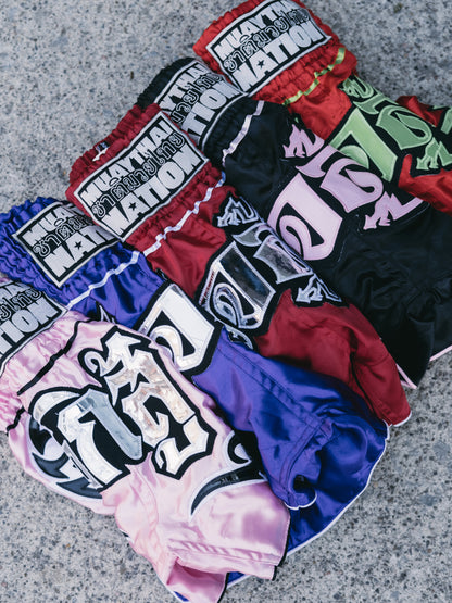 Collection of blue, red, black, pink Muay Thai shorts with white muay thai nation logo. 