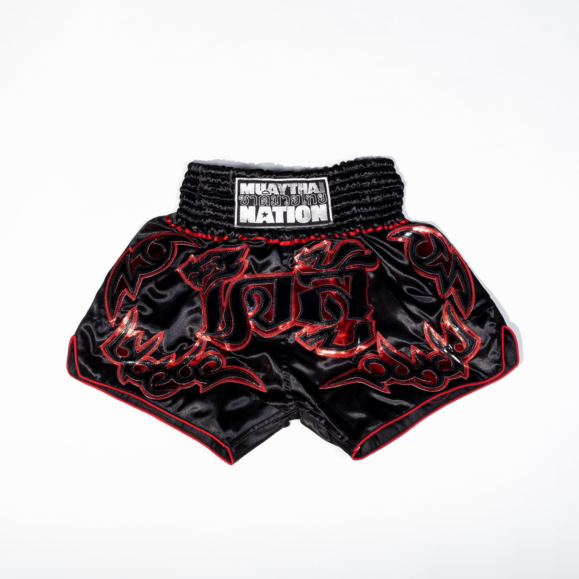 A pair of Muay Thai shorts featuring a satin fabric with a red, green, and white color scheme. The shorts have floral patterns and text that reads 'Muay Thai Nation' and 'BANGKOK'.