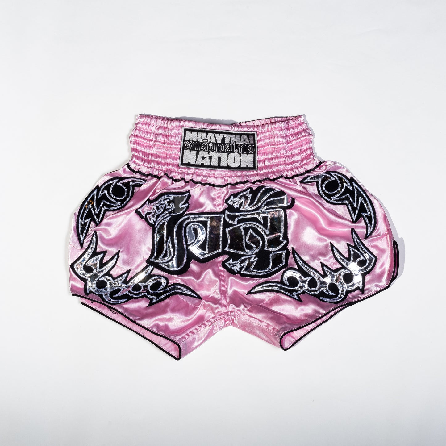 A pair of Muay Thai shorts featuring a satin fabric with a red, green, and white color scheme. The shorts have floral patterns and text that reads 'Muay Thai Nation' and 'BANGKOK'.