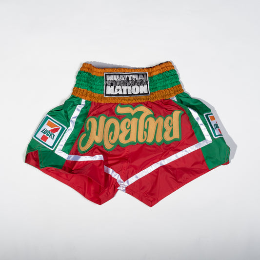 Muay Thai Nation limited edition Lucky 7 red and green satin shorts featuring gold Thai script lettering and a retro convenience store patch design