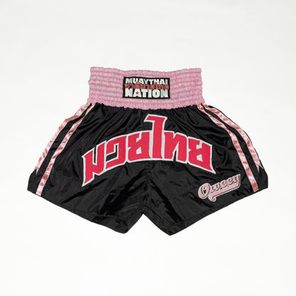 Black and pink Muay Thai shorts with visible branding on a white background
