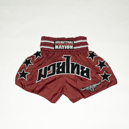 Red Muay Thai shorts with star patterns and 'Nation' branding on a white background
