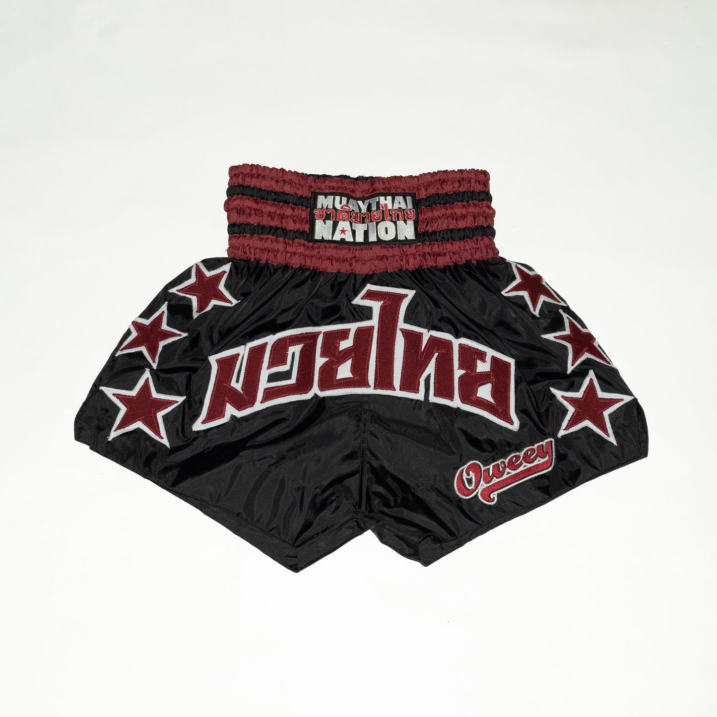 Black Muay Thai shorts with red accents and star patterns on a white background