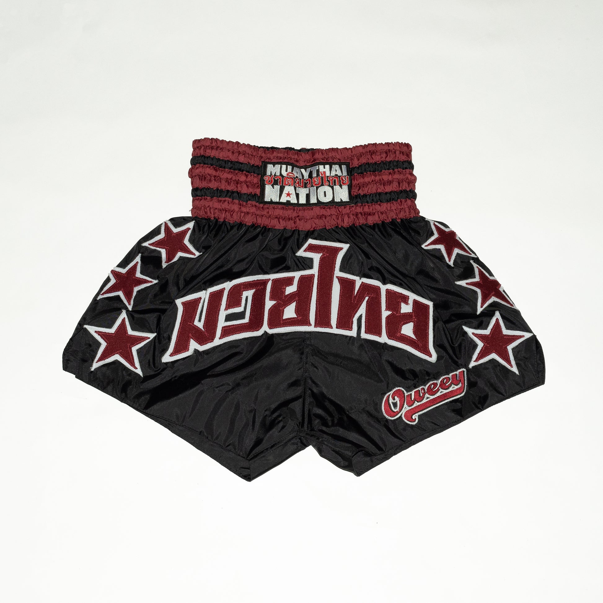 Black Muay Thai shorts with red accents and star patterns on a white background