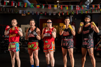 Muay thai fighters wearing red, green and black muay thai shorts paired with black and red tank tops.